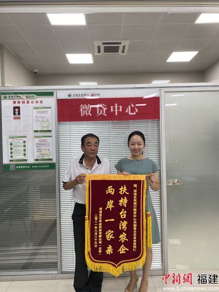 台商邓育承把一面写着“扶持台湾农企两岸一家亲”的锦旗递到漳浦农商银行。